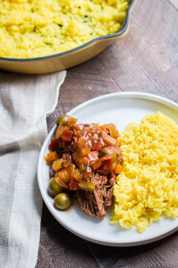 white plate with ropa vieja and sauce and yellow rice.