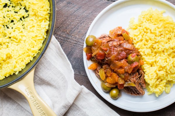 Skillet of yellow rice, and a plate of ropa vieja and yellow rice.