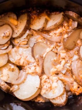 sliced potatoes with cheese and onions in a slow cooker.