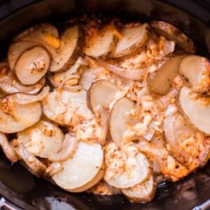 sliced potatoes with cheese and onions in a slow cooker.