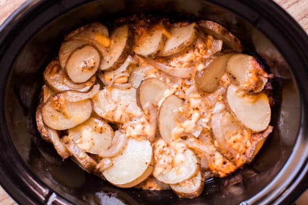 sliced potatoes with cheese and onions in a slow cooker.