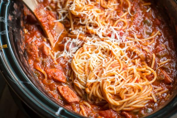 close up of spaghetti in a slow cooker with a wooden spoon in it.