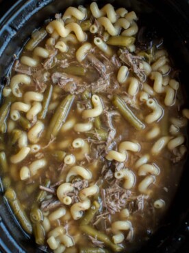 French dip shredded beef soup in slow cooker with curly noodles.