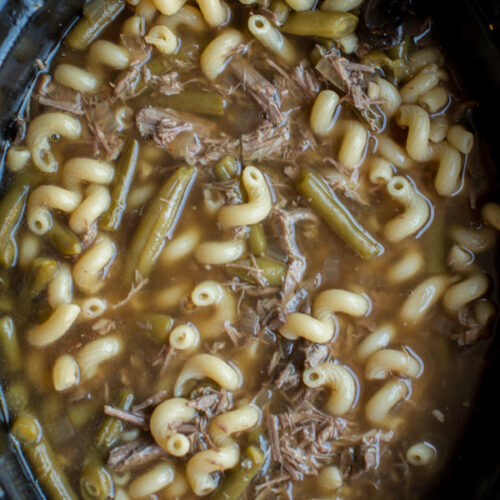 French dip shredded beef soup in slow cooker with curly noodles.