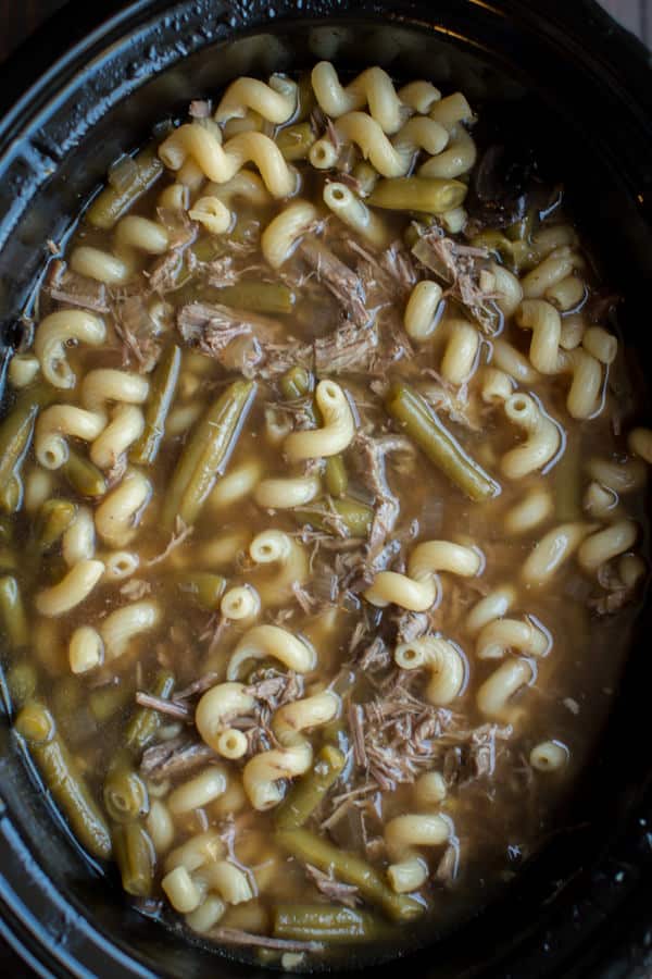 French dip shredded beef soup in slow cooker with curly noodles.