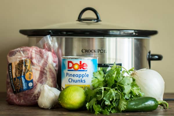 pork roast, pineapple chunks, cilantro, onion, garlic in front of a slow cooker.