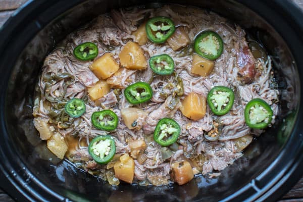 shredded pork in a slow cooker with pineapple chunks and jalapeno slices.