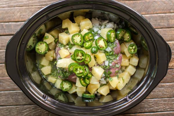 uncooked pork, pineapple, onion and jalapenos in a slow cooker.