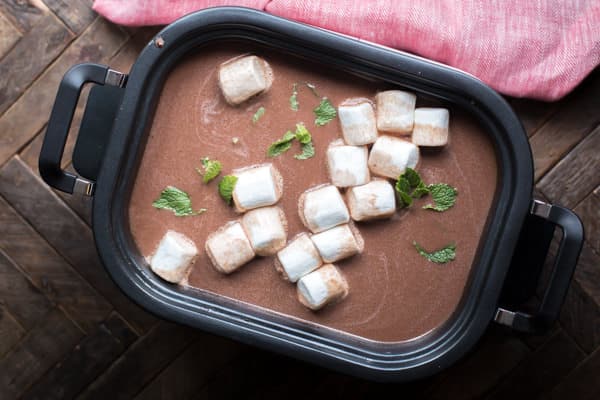 slow cooker filled with mint hot chocolate and large marshmallows on top.