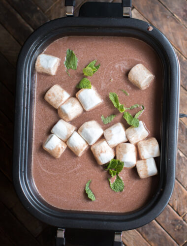 mint hot chocolate in slow cooker with mint and marshmallows on top.