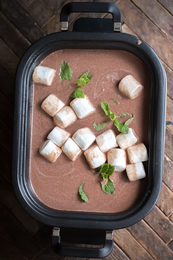 mint hot chocolate in slow cooker with mint and marshmallows on top.