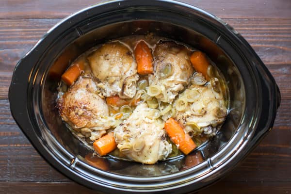 chicken thighs in sauce in a slow cooker with leeks and carrots.