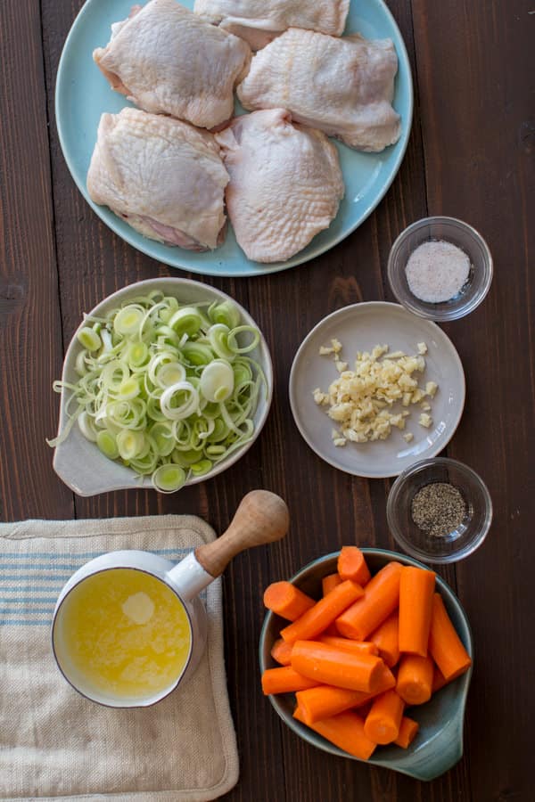 chicken thighs, garlic, salt and pepper, carrots and butter on a wooden table.