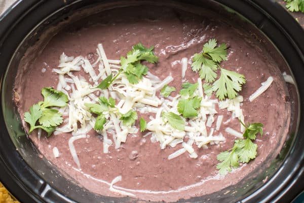 close up of refried black beans in a slow cooker with cheese and cilatnro on top.