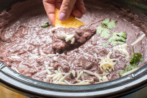 Refried black beans being scooped from a slow cooker on a chip.