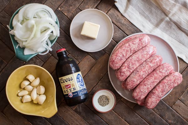 brats, onion, garlic, beer and butter on a wooden table.