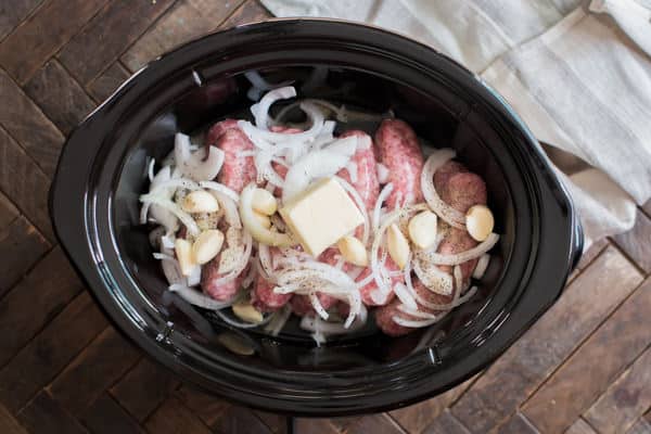 raw brats, onion, garlic and butter in a slow cooker not yet cooked.