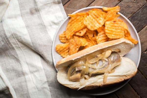 beer brat on a bun with barbecue chips on the side.