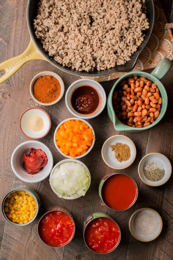 ground beef, chipotle peppers, pinto beans, tomatoes, and seasonings on a wooden table.