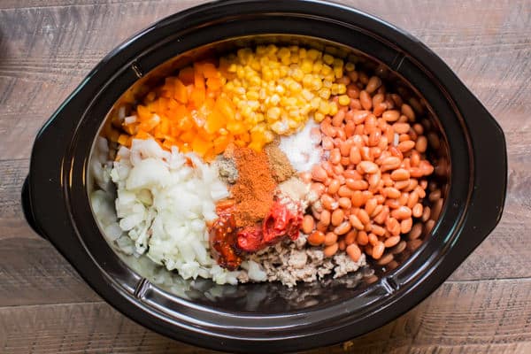 onion, bell pepper, corn, pinto beans and ground beef in a slow cooker not yet cooked.