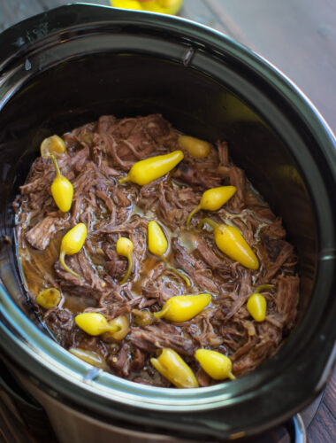 shredded meat in a slow cooker with peppers on top.