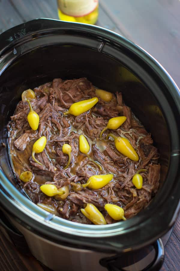 shredded meat in a slow cooker with peppers on top.
