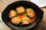 5 stuffed peppers in a tomato sauce in a slow cooker