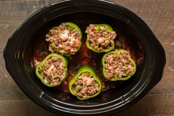 uncooked stuffed peppers on top of marinara sauce in slow cooker.