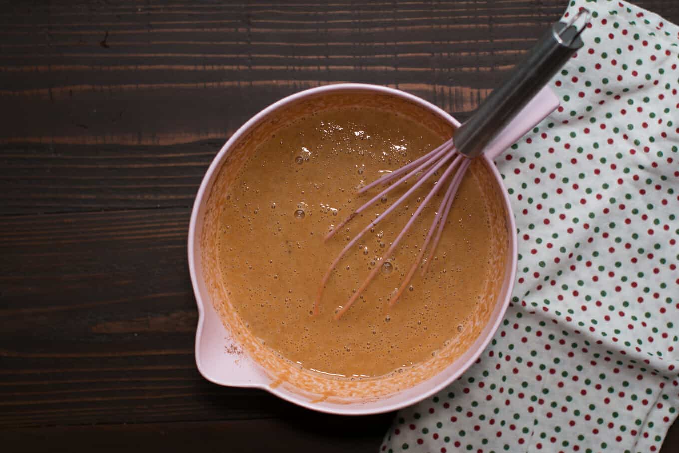 pumpkin pie filling in a pink bowl with a pink whisk in it.