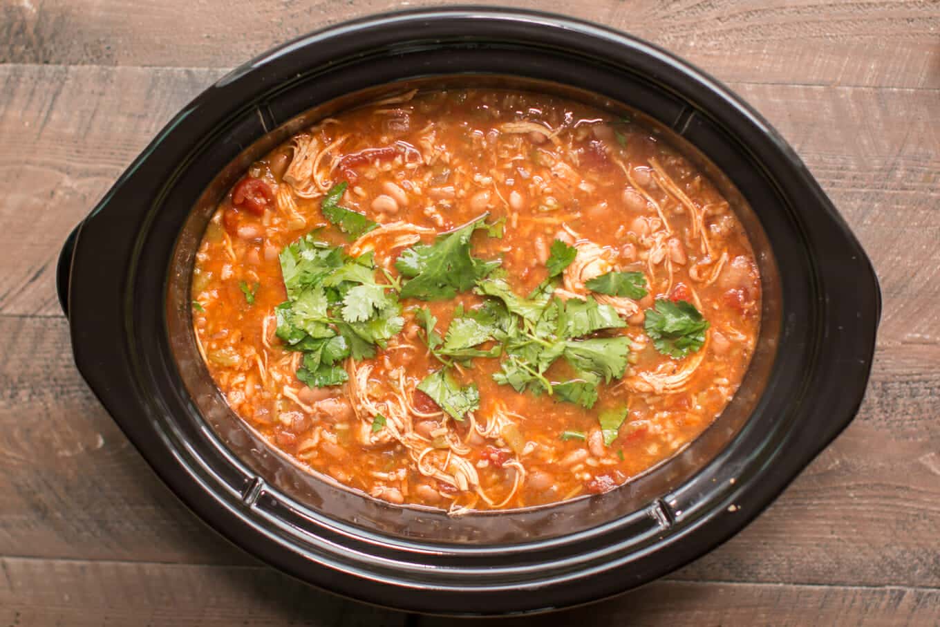 tomato based chicken soup garnished with cilantro in a slow cooker