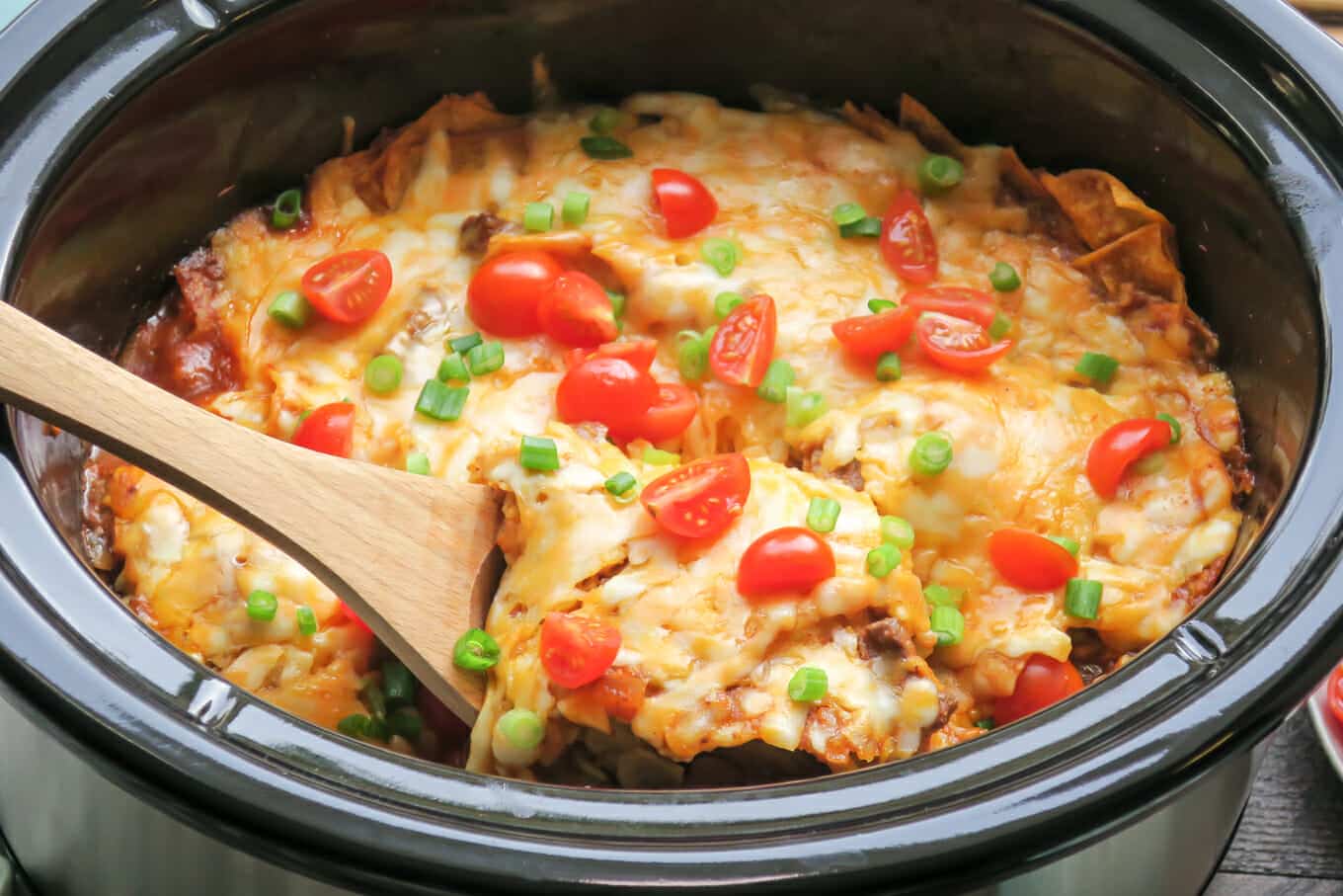 close up of enchilada casserole in slow cooker with wooden spoon in it.
