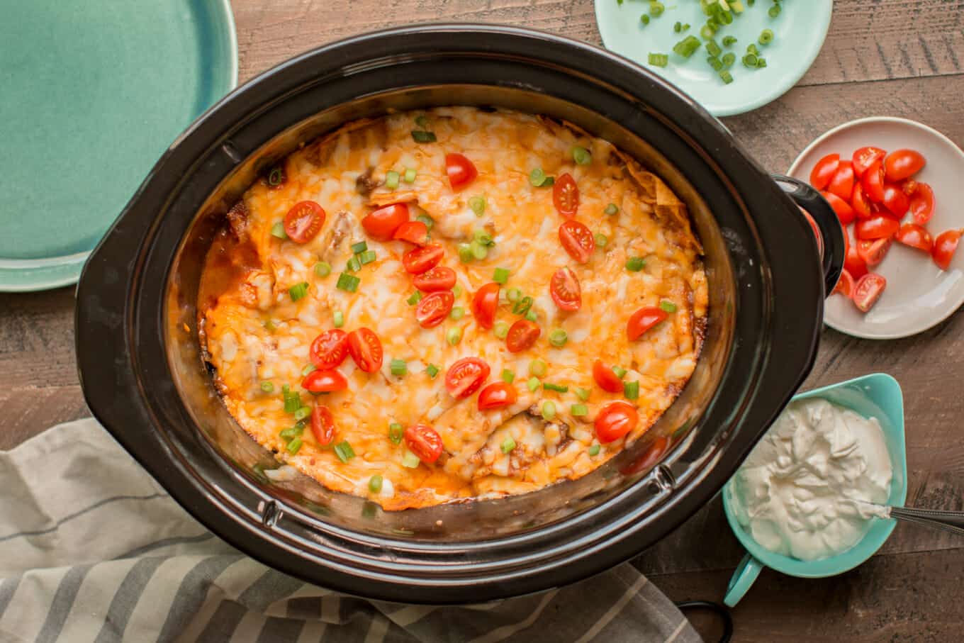 beef enchilada casserole in slow cooker with sour cream on the side.