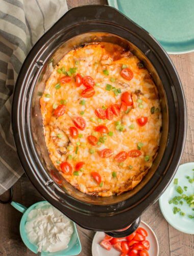 Enchilada casserole in slow cooker with tomatoes and green onion on top.