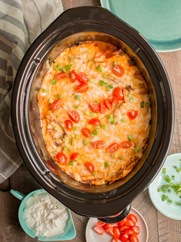 Enchilada casserole in slow cooker with tomatoes and green onion on top.