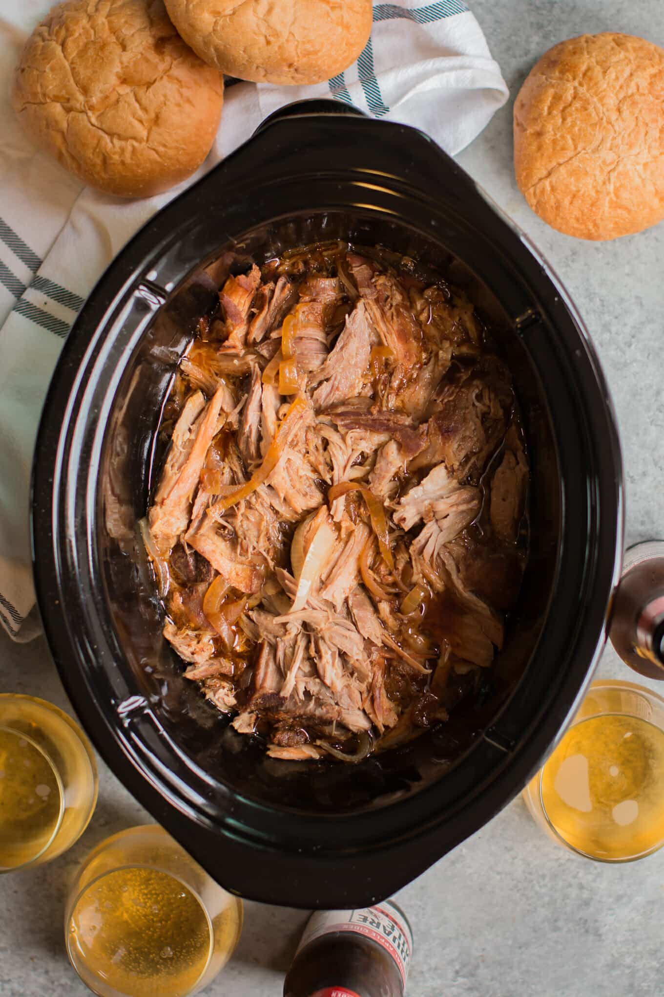 shredded pork in slow cooker with hard ciders in glasses on the side.