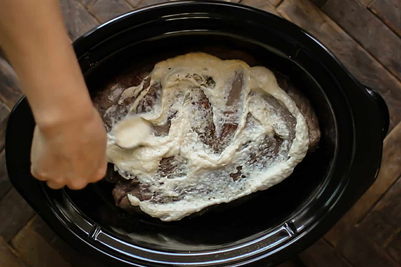 horseradish being spread on top of a browned roast.