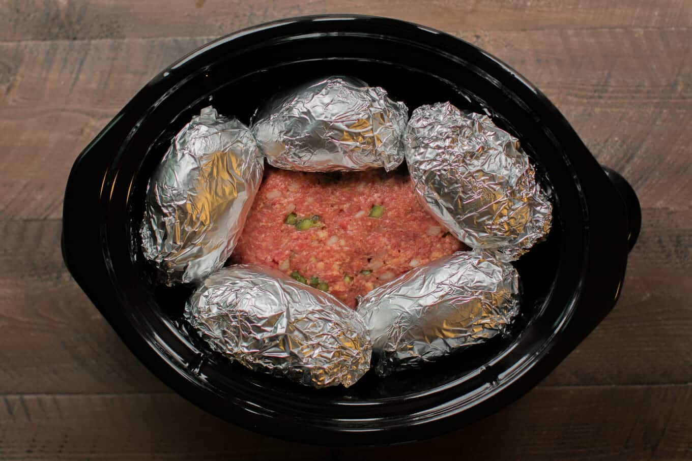 raw meatloaf in slow cooker, 5 potatoes wrapped in foil on top