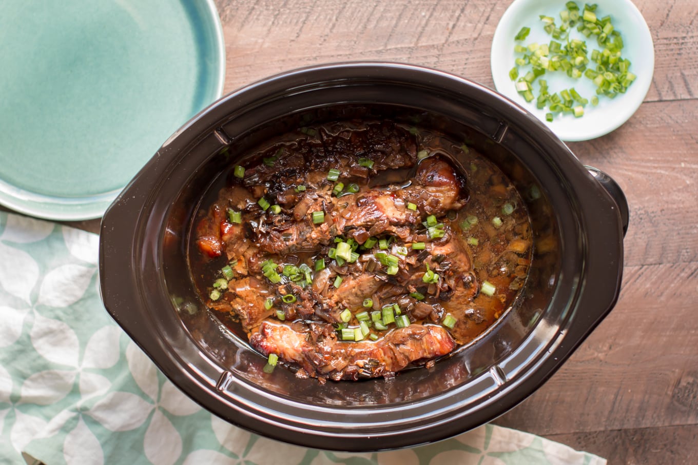 country style ribs in molasses sauce in slow cooker with green onions on top.