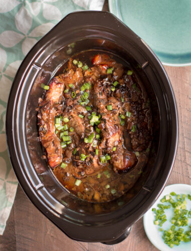 cooked ribs in sauce with green onions on top.