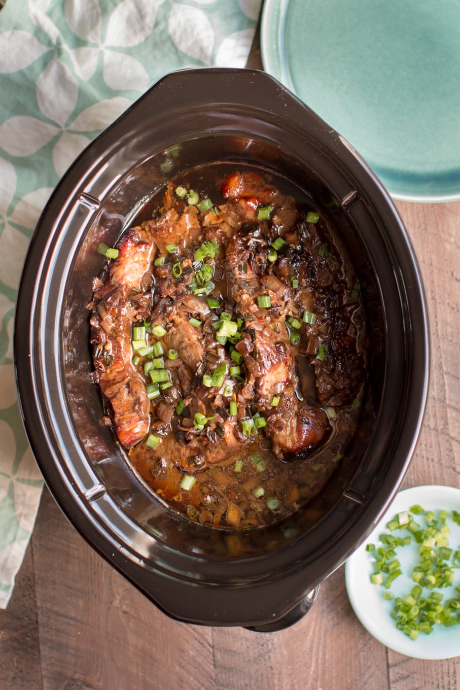 cooked ribs in sauce with green onions on top.