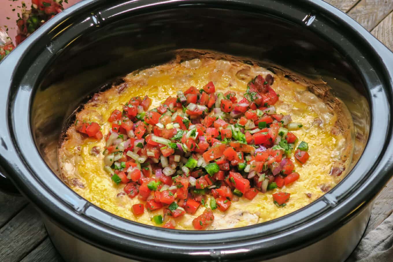 bean dip with cheese and salsa on top in the slow cooker.