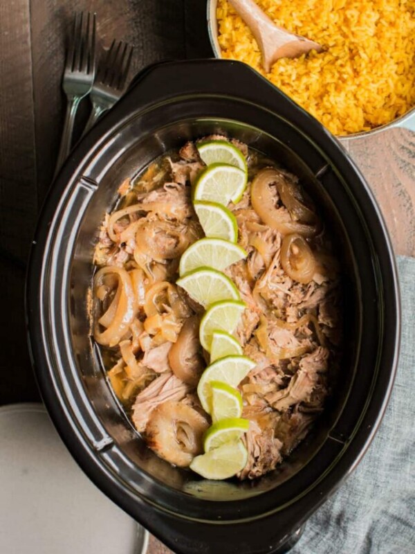 cuban pork in slow cooker with onion and limes on top.