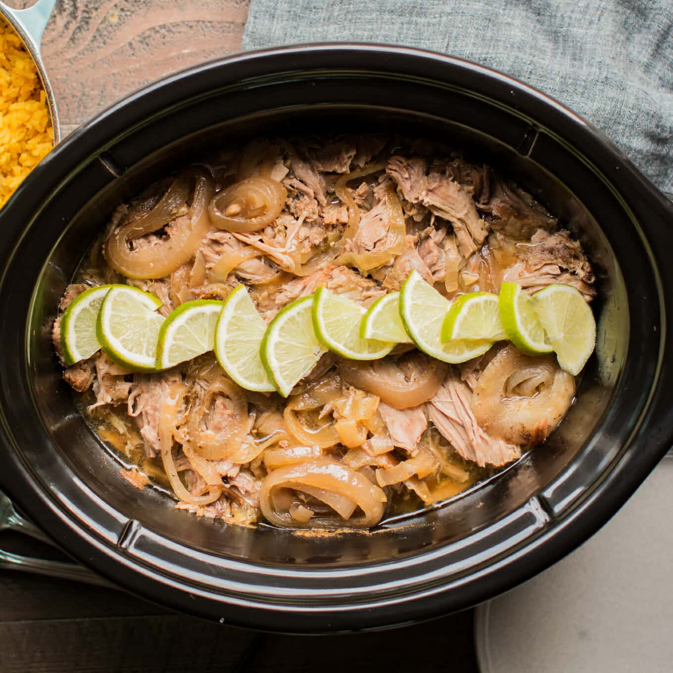 top view of shredded Cuban pork in slow cooker garnished with limes