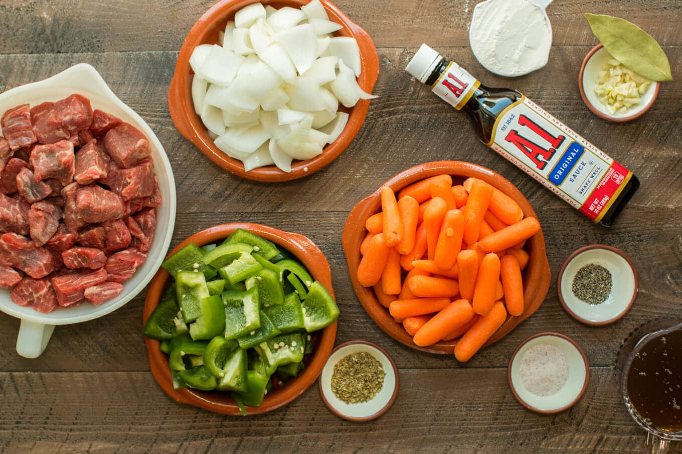 raw beef cubes, bell pepper, carrots, onion, bell pepper and A1 sauce on wooden cutting board.