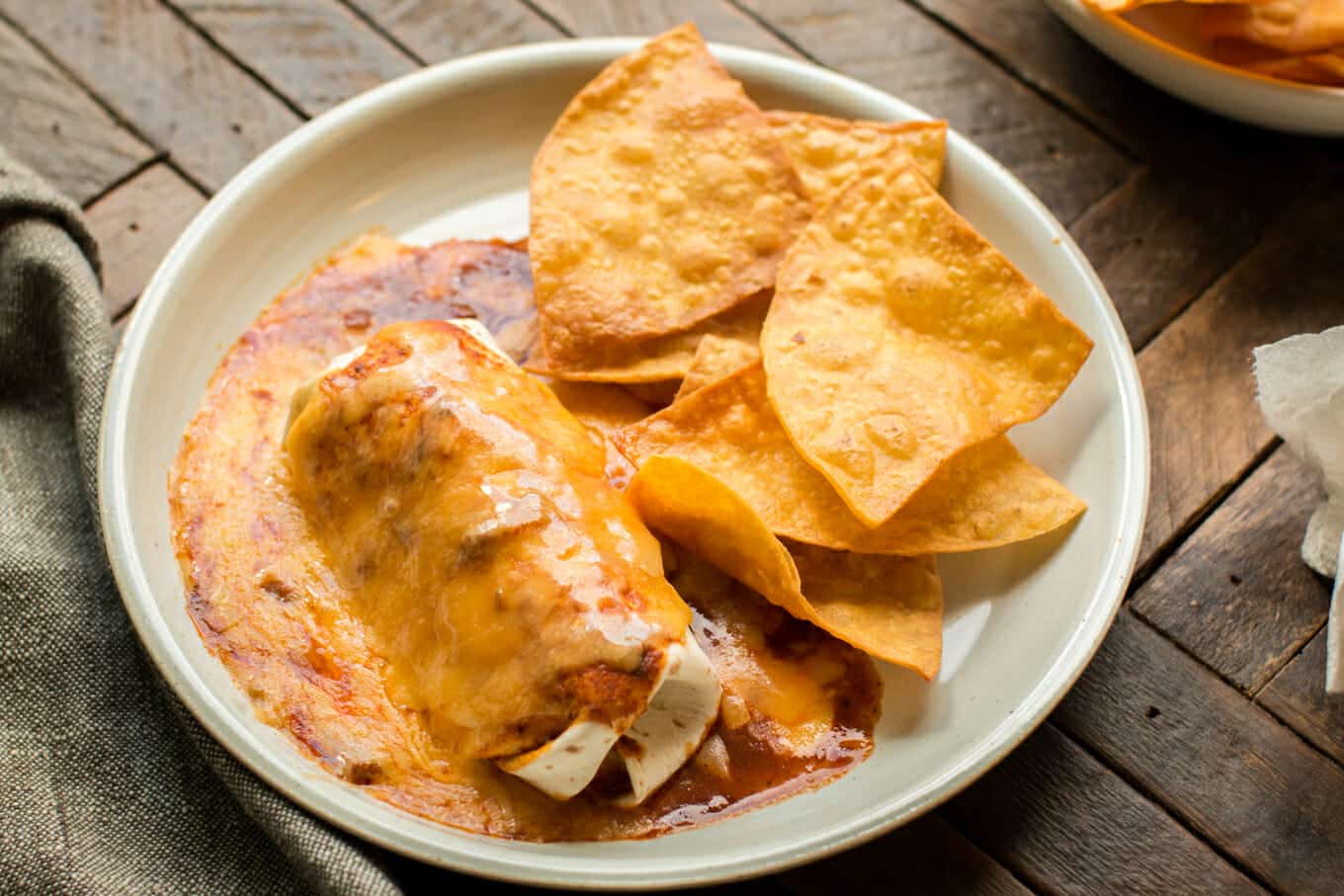 beef burrito with red enchilada sauce on top on plate with chips on the side.