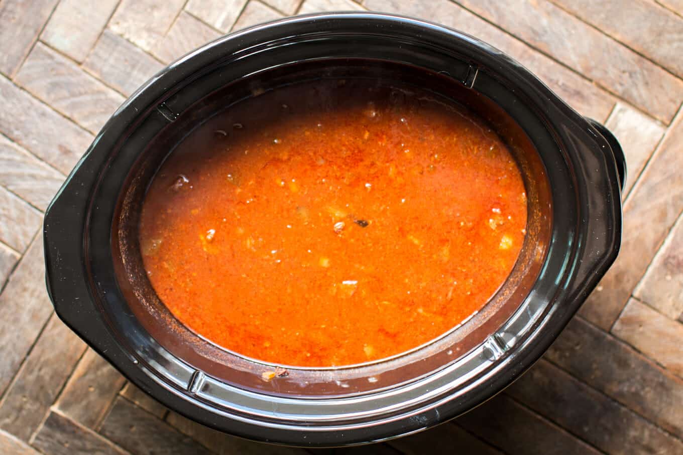 cooked beef in red enchilada sauce in slow cooker.