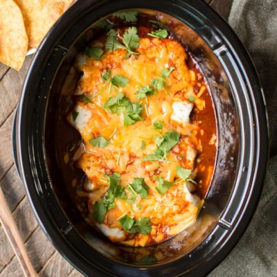 4 large burritos in red sauce and cheese on top in slow cooker.