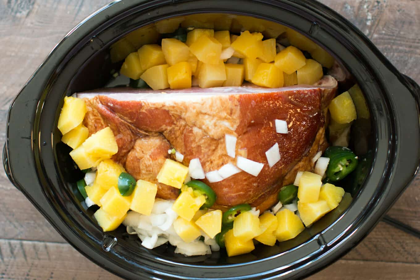 Ham in slow cooker with pineapple, onion and jalapeno on top. Uncooked.