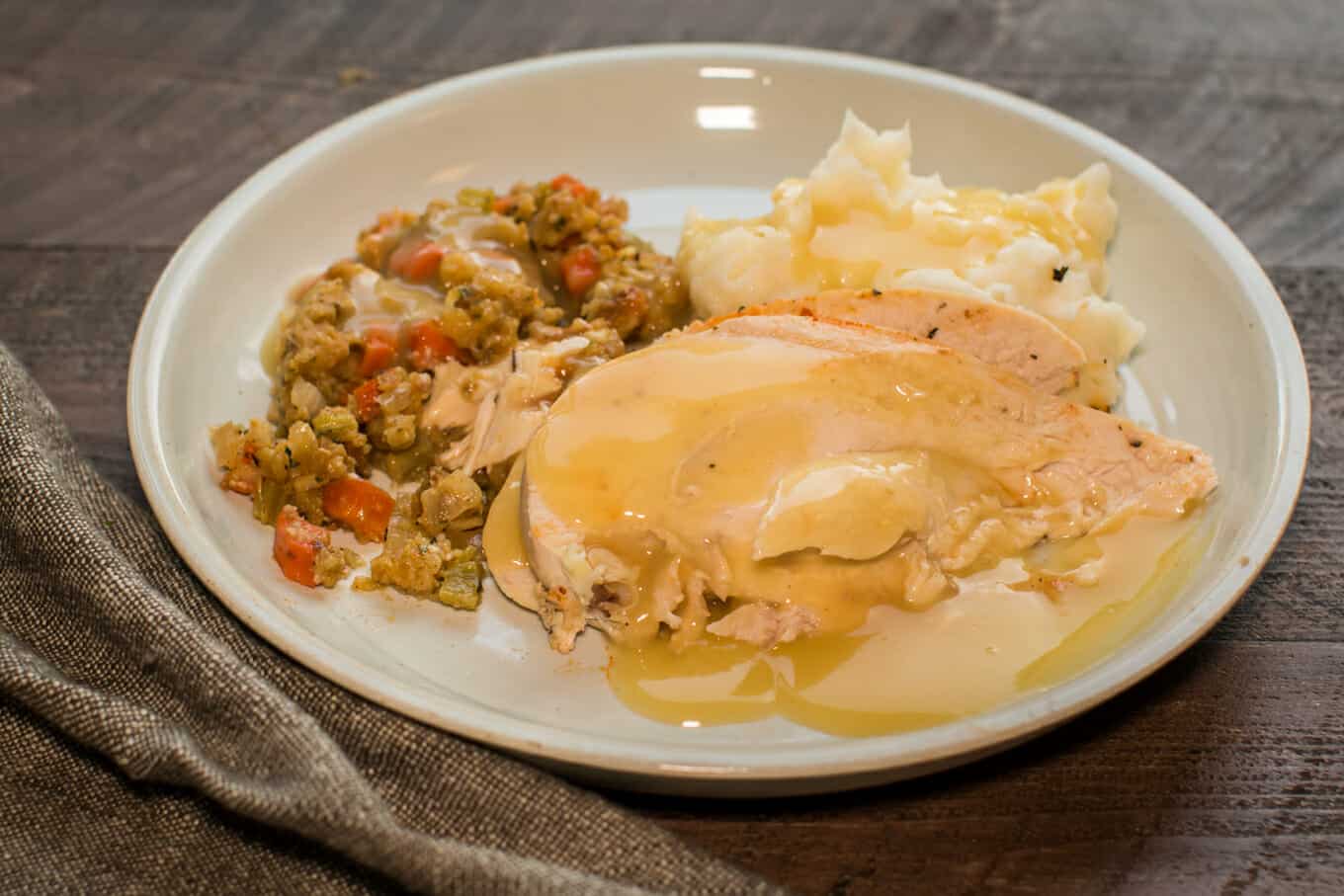 sliced chicken with stuffing and mashed potatoes on a grey plate.