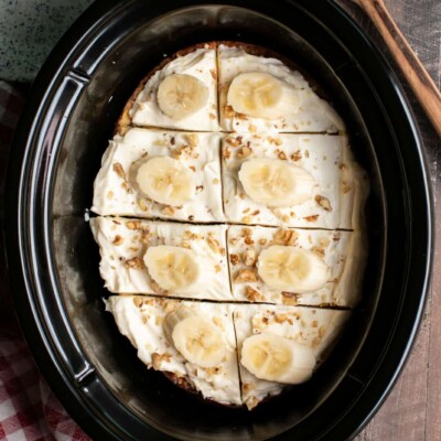 Banana cake in slow cooker with cream cheese frosting and banana slices on top.
